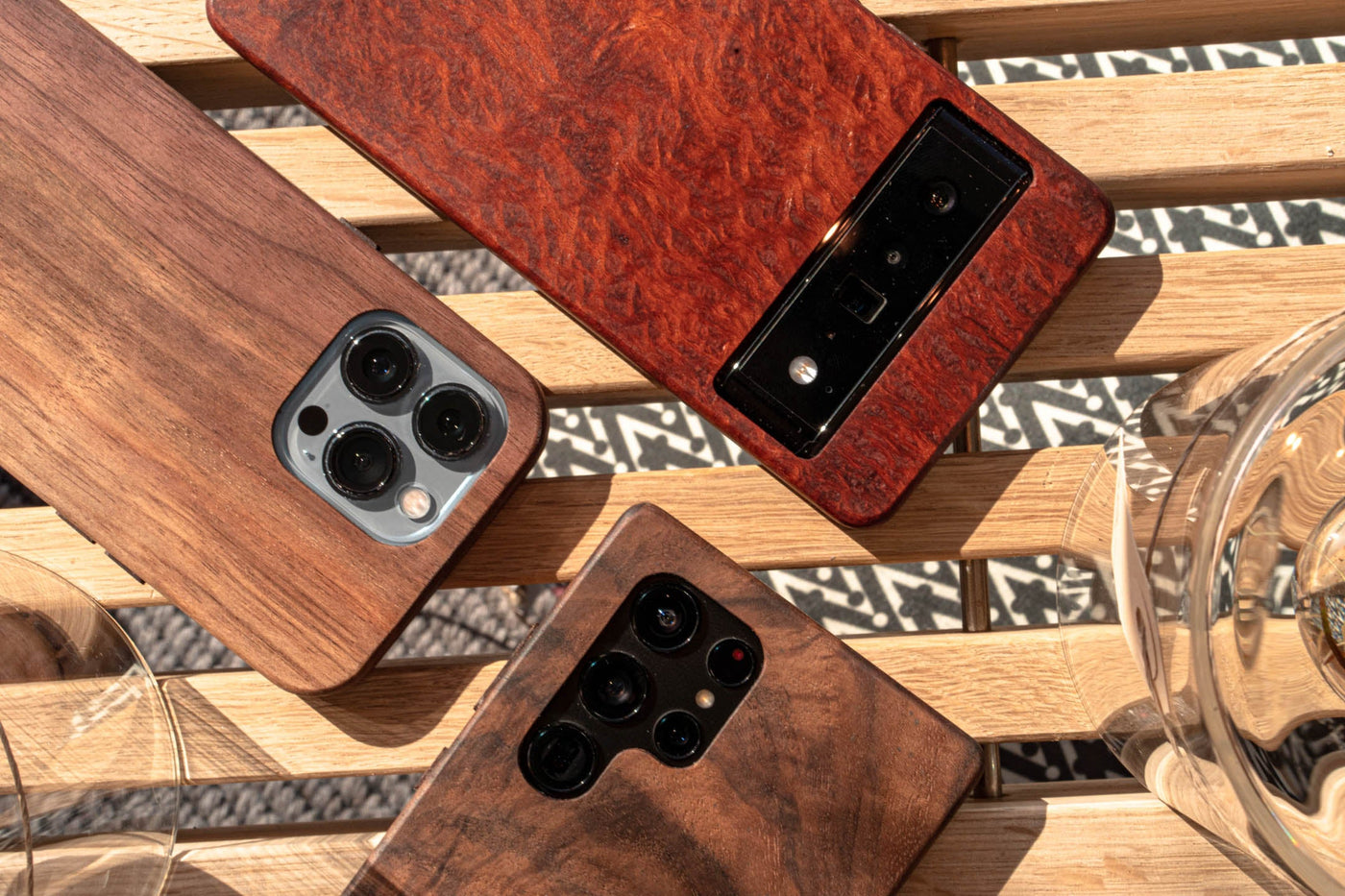 three wooden phone cases sitting on a wood bench in daylight