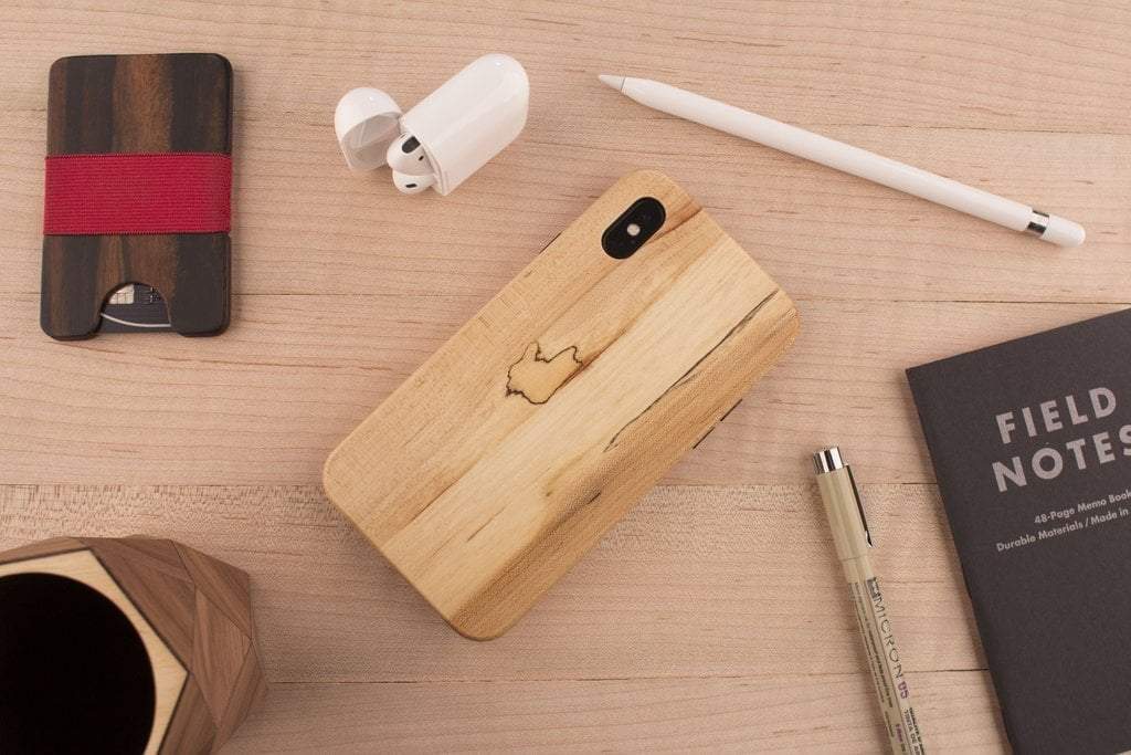 a wooden phone case on a table with airpods, an apple pencil and notebook